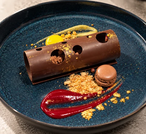 A sculpted chocolate dessert and a macaron on a deep blue plate.